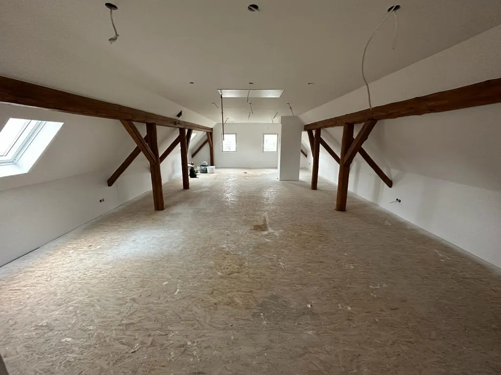 Dachgeschosswand mit sichtbaren Holzbalken und passgenauem Trockenbauabschluss