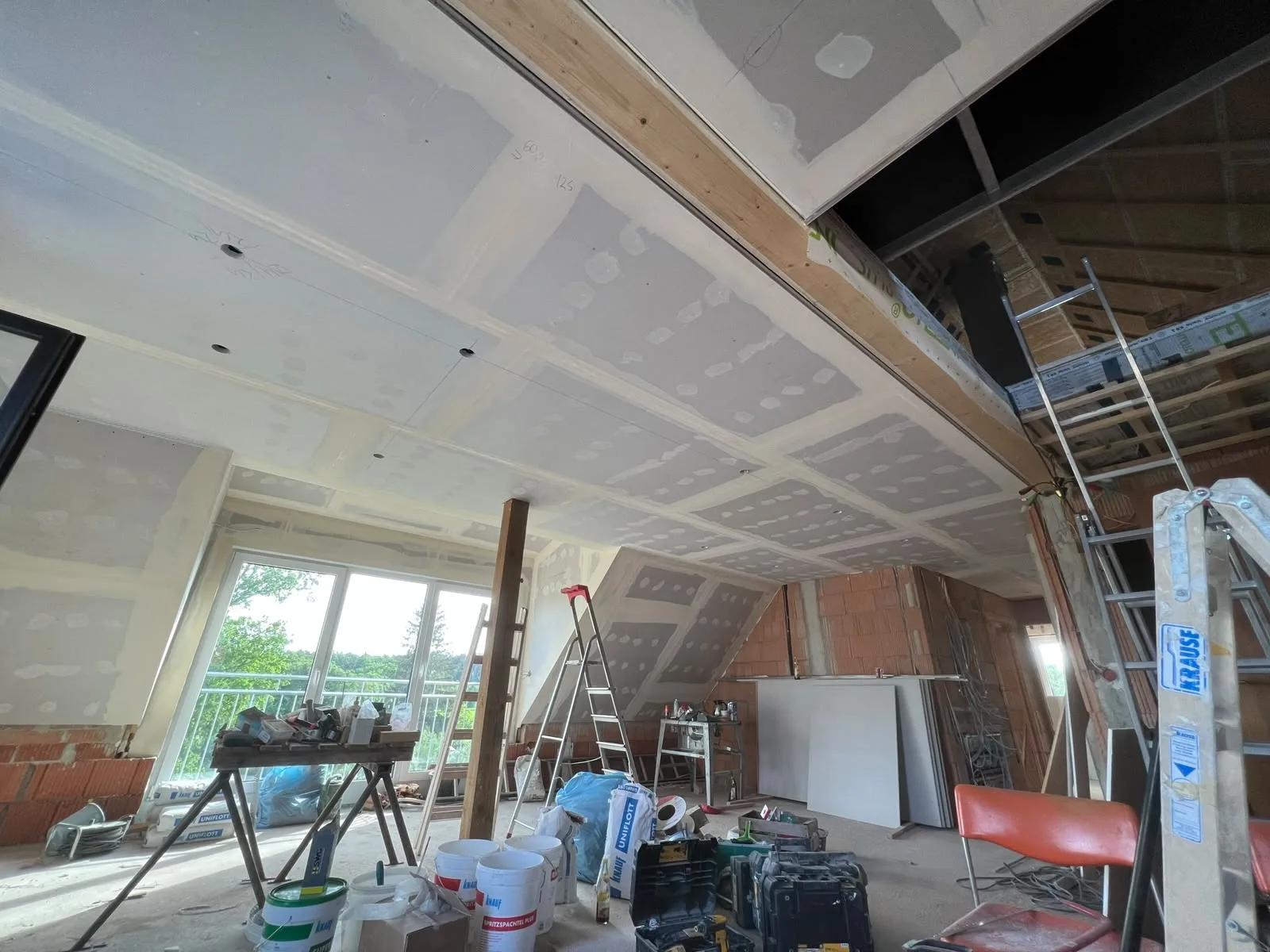 Dachgeschoss im Ausbau mit großflächig verspachtelter Decke zwischen sichtbaren Holzbalken