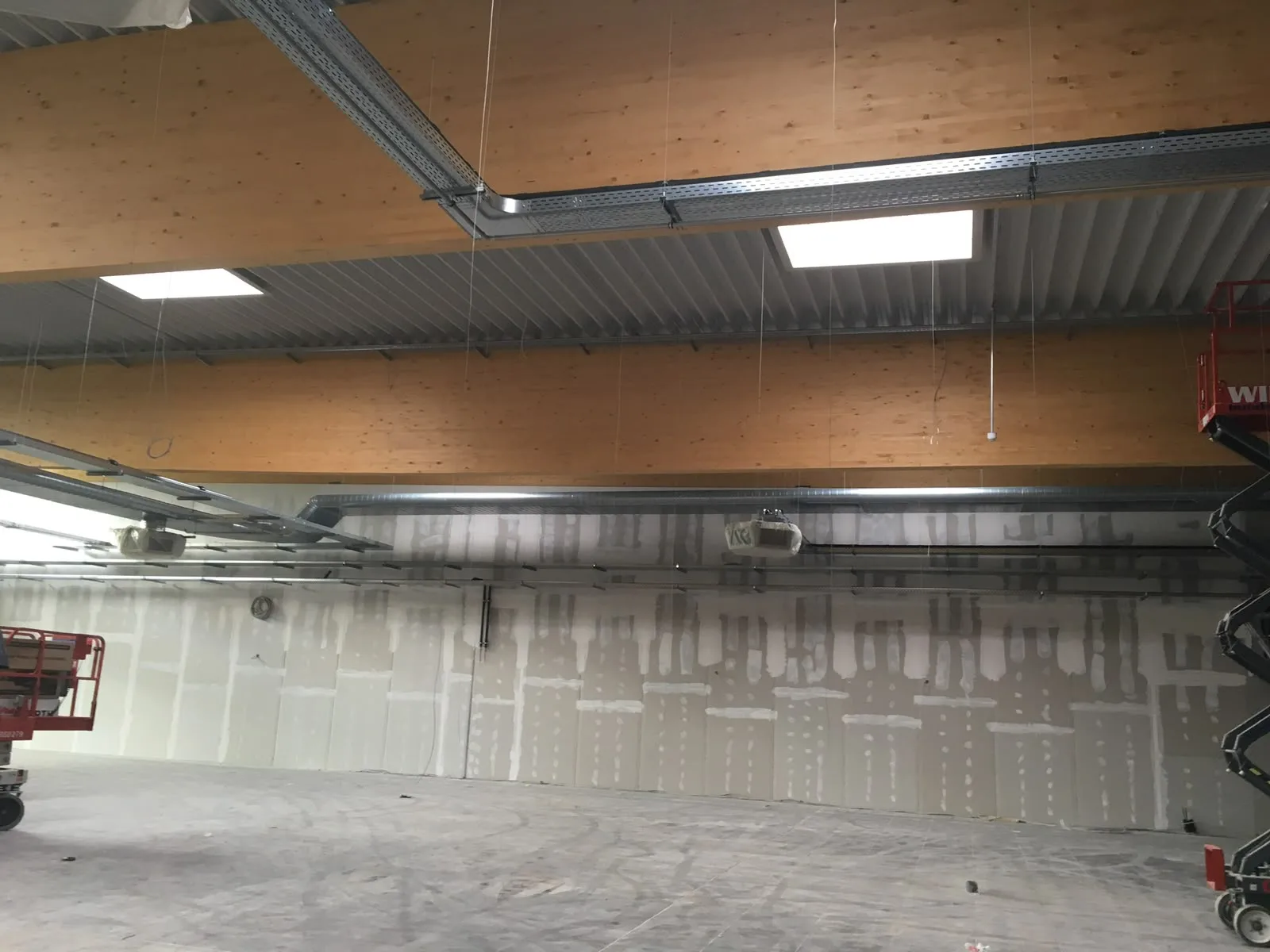 Verspachtelte Hallenwand unter Holzbindern mit abgehängten Lüftungs- und Elektrotrassen